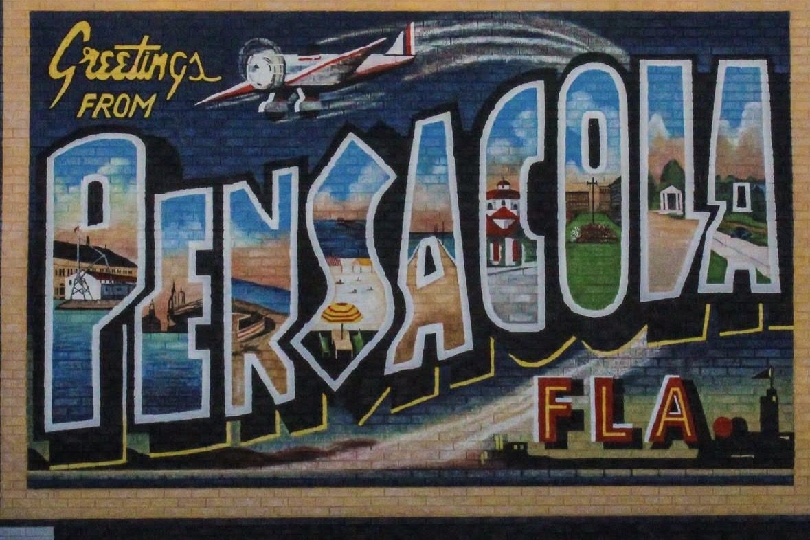 A vintage-style Greetings from Pensacola mural painted on a brick wall
